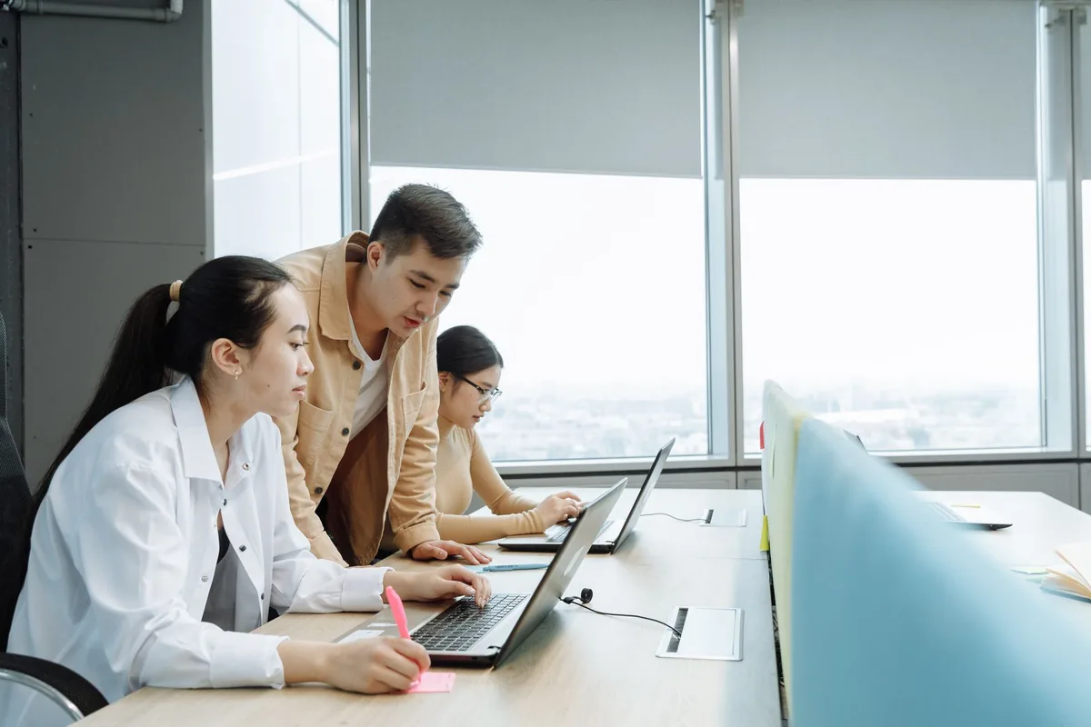 Three people exchanging ideas around a table with their laptops